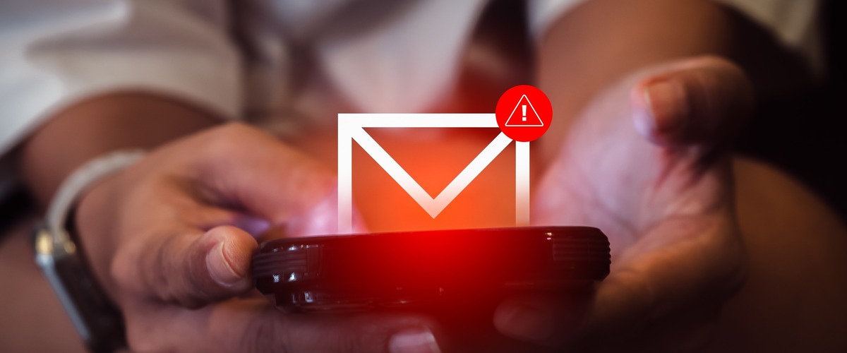 Zwei Hände halten ein Smartphone, über dem ein Mail-Symbol mit Warnhinweis schwebt